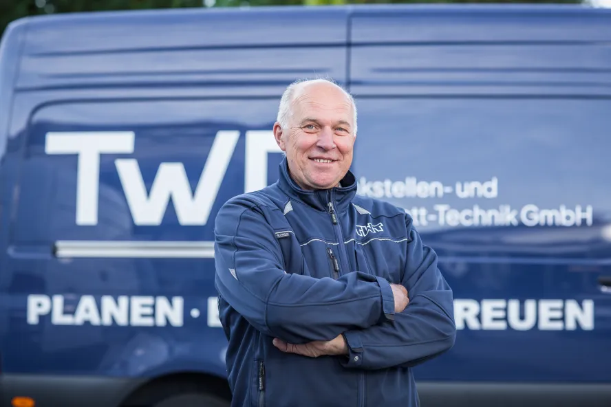 Günter Mirbach steht vor einem blauen Transporter der TWT