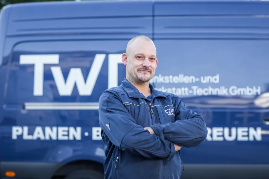 Manuel Holländer steht vor einem blauen Transporter der TWT