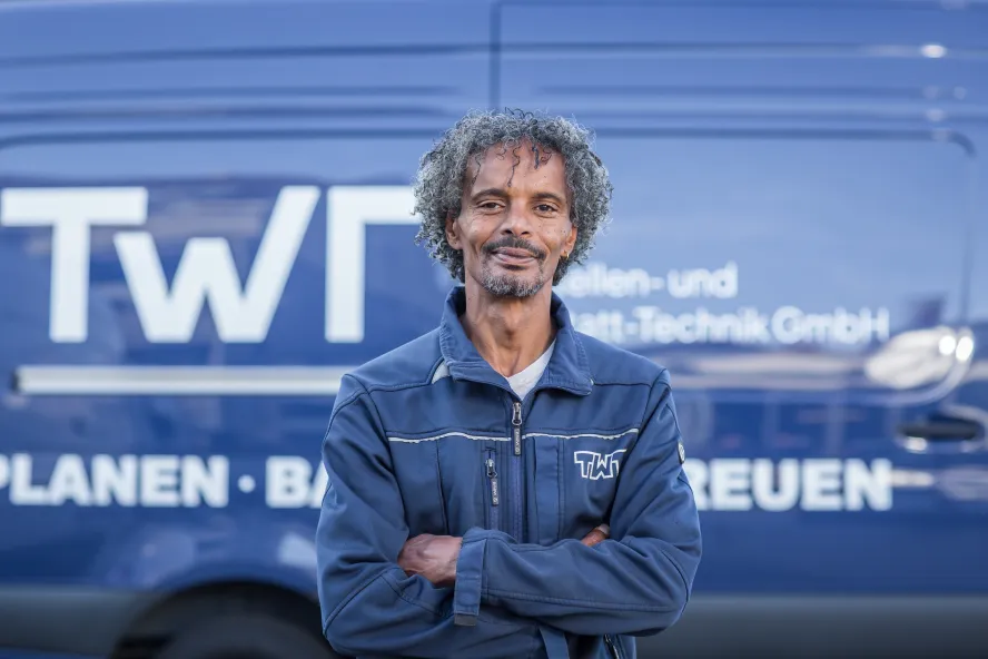 Yonas Ghirmay steht vor einem blauen Transporter der TWT