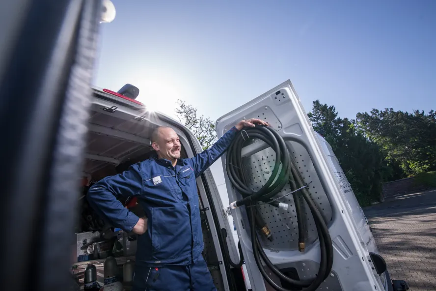 Eine TWT-Mitarbeiterin in blauer Arbeitskleidung steht neben der geöffneten Tür eines Transporters. 